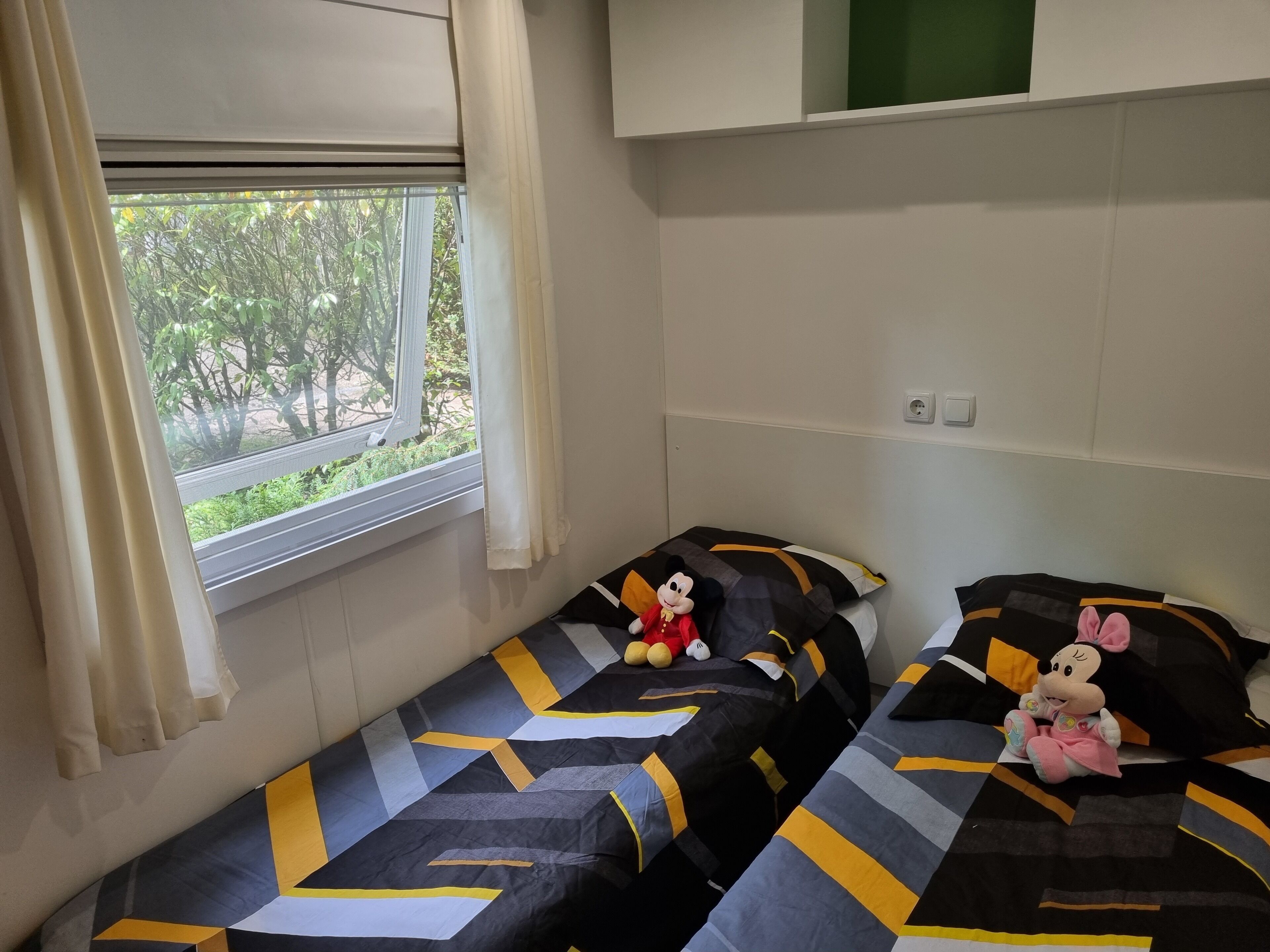 Eine kleine, einfache Unterkunft mit zwei Einzelbetten, jedes mit einem Mickey Mouse Kuscheltier.
