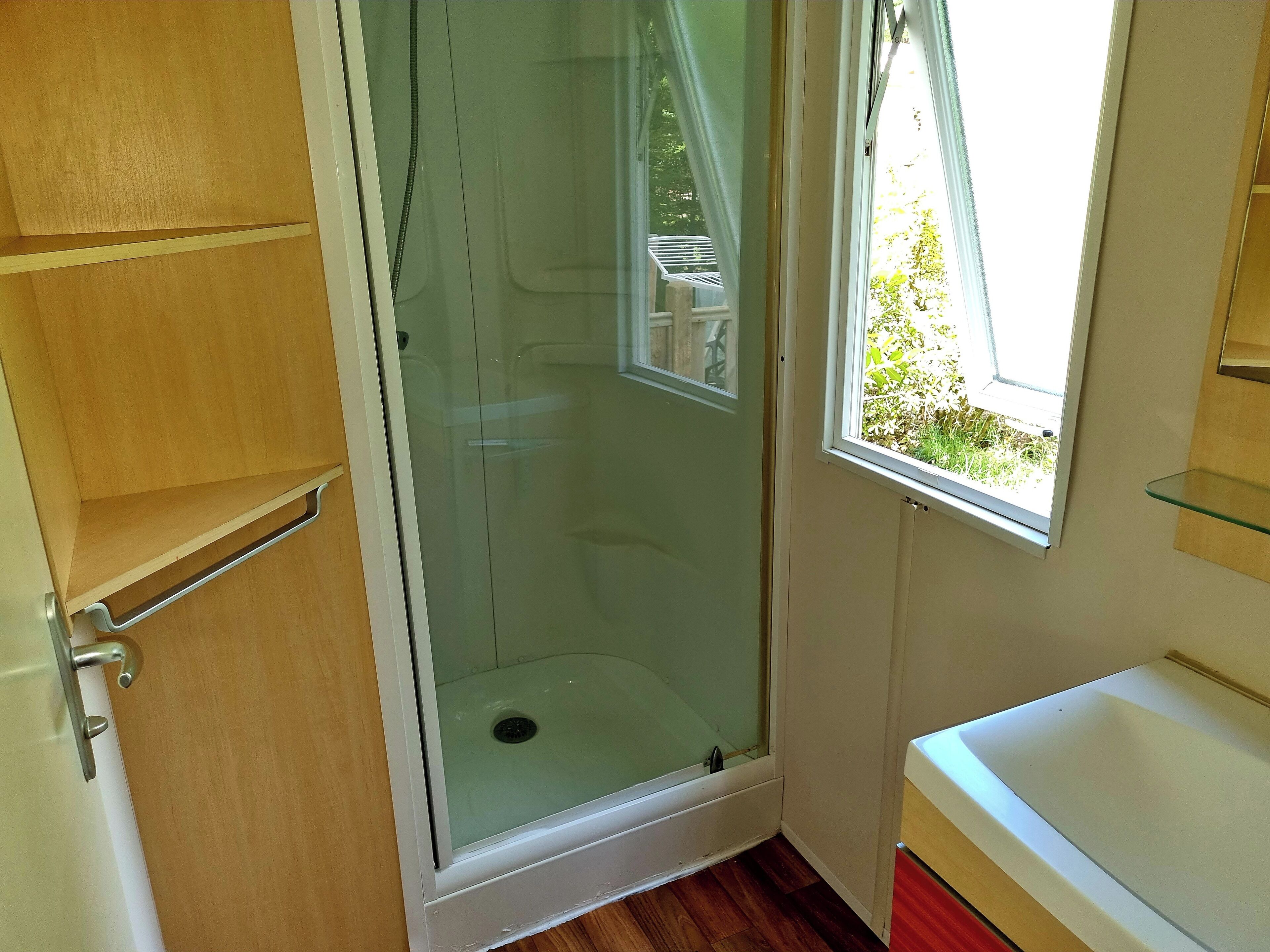 A bathroom with a glass shower enclosure, a window, and a wooden cabinet.