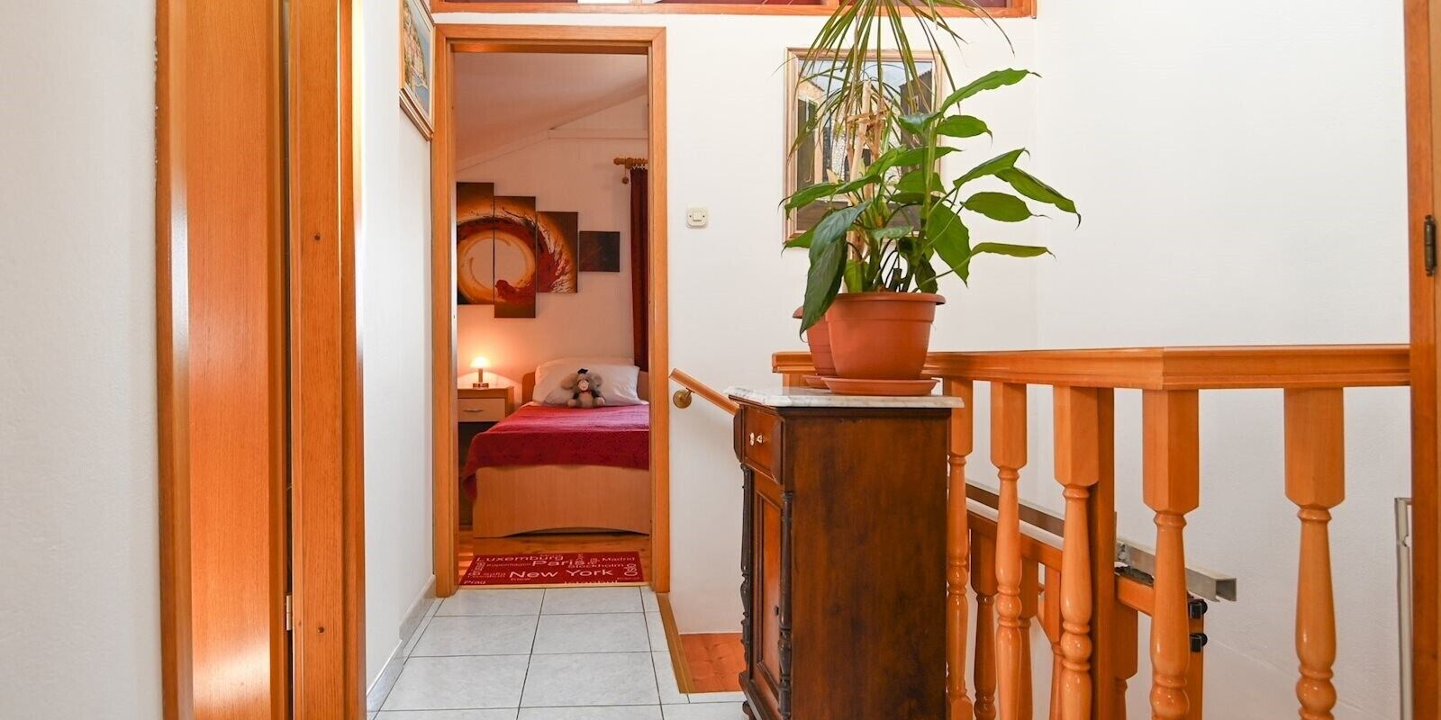 Ein Flur, der in ein Schlafzimmer mit einem Bett, einem Nachttisch, einer Lampe und einem Blumentopf führt.