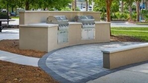 Zona de barbacoa amb graelles integrades, un camí de pedra corbat i una banca.