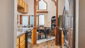 A kitchen with wooden cabinets, a dining area, and a large refrigerator. - Amazing Views! Jacuzzi-Sauna-Firepit-Arcades-Game Room-King Beds-Walk to Schuss (Bellaire)