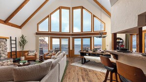 A spacious living area with a high ceiling, large windows, a stone fireplace, and a cozy seating arrangement. - Amazing Views! Jacuzzi-Sauna-Firepit-Arcades-Game Room-King Beds-Walk to Schuss (Bellaire)