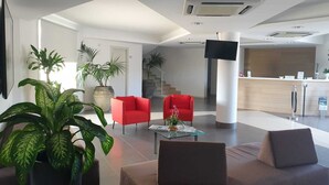 Un vestíbulo moderno con una recepción, dos sillones rojos, un sofá marrón y plantas en macetas.