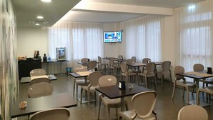 Un salón de conferencias con mesas, sillas, una pantalla de televisión y un refrigerador.