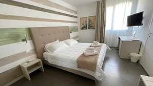 Habitación de hotel con una cama grande, una mesita de noche, un televisor y un escritorio con una silla.