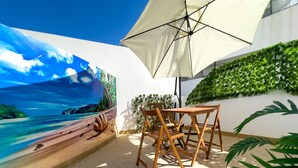 Un patio con una mesa y sillas de madera, un gran paraguas y un mural con una escena de playa.