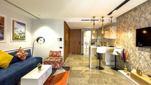 Una sala de estar moderna con sofá, una mesa de centro y un tapete estampado. Hay una zona de cocina con una mesa de comedor y taburetes de bar.