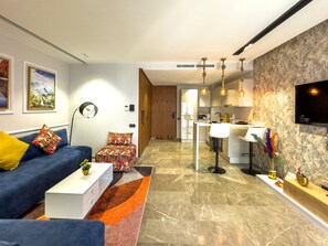 A modern living room with a sofa, coffee table, and a patterned rug. There is a kitchen area with a dining table and bar stools. - Modern & Fully Equipped Studio in Princesses Maarif -Pavillon 12- (Casablanca)