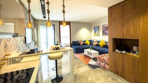 Una cocina moderna con una isla central, un comedor con sofá azul y cojines amarillos, y un mueble de madera con vajillas de té.