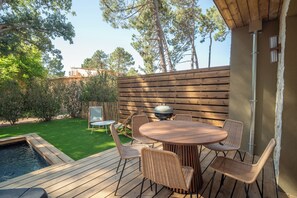 Eine Holzterrasse mit rundem Tisch, Korbstühlen, einem Grill und einem kleinen Pool.