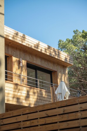 Ein modernes Holzgebäude mit großen Fenstern, einem Balkon und einem weißen Sonnenschirm.