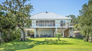Une maison à deux étages avec un grand garage, un espace extérieur aménagé avec un coin salon couvert et une pelouse bien entretenue.
