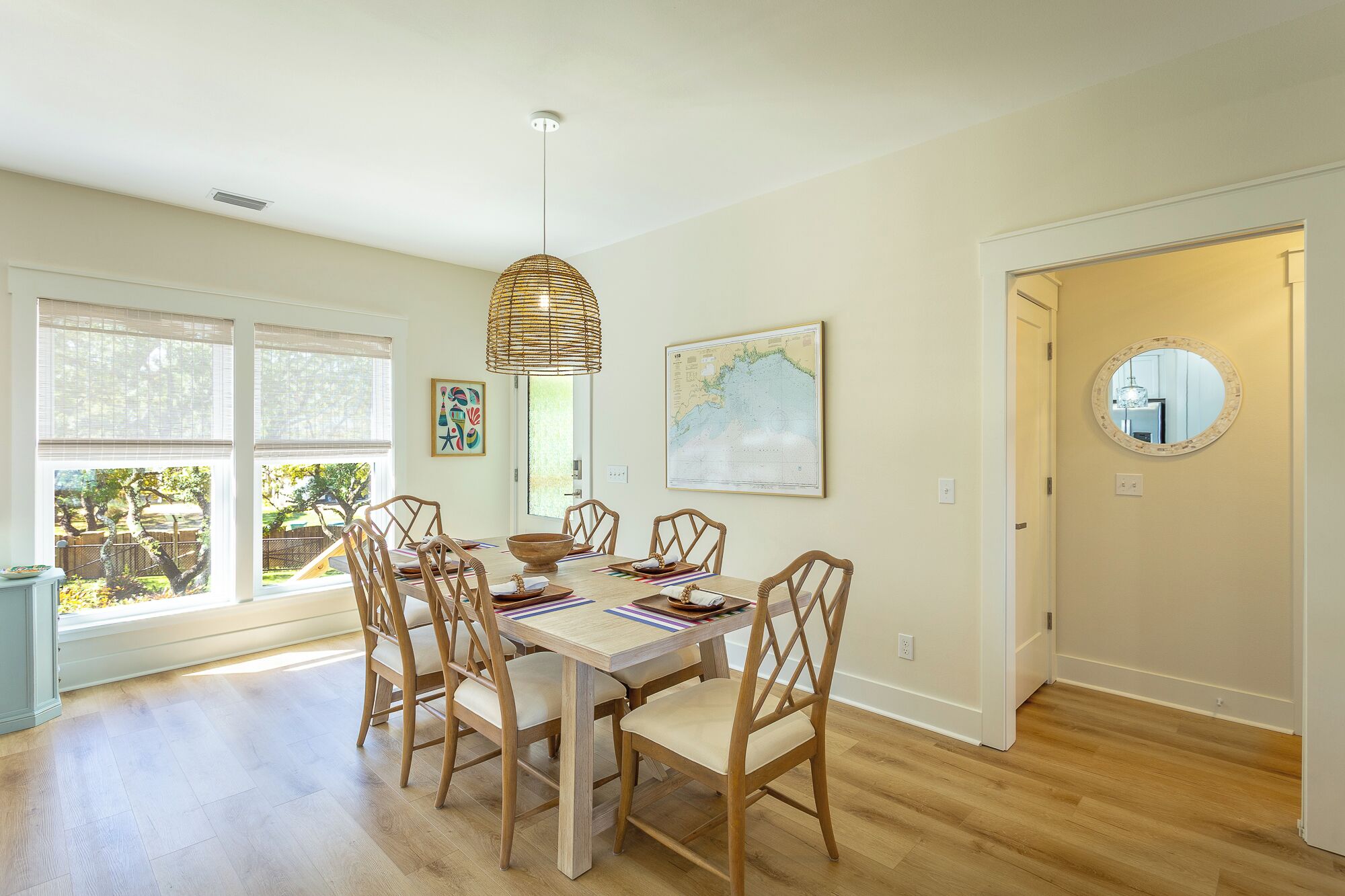A dining area with a wooden table and chairs, a hanging light fixture, a map on the wall, and a door with a mirror.