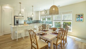 Une cuisine moderne avec des armoires blanches, des appareils en acier inoxydable et un coin repas comprenant des chaises et une table en bois.