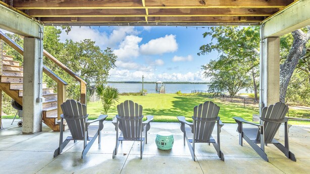 Une terrasse couverte, dotée de fauteuils Adirondack et offrant une vue sur un lac.