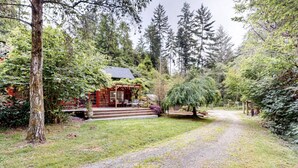 A rustic cabin with a porch, surrounded by dense forest and a gravel path. - Lucky Clover over the Covered Bridge (Eureka)