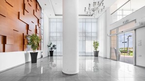 En rymlig entréhall med modern design, med en stor pelare, krukväxter och utsikt över omgivningen genom stora fönster.