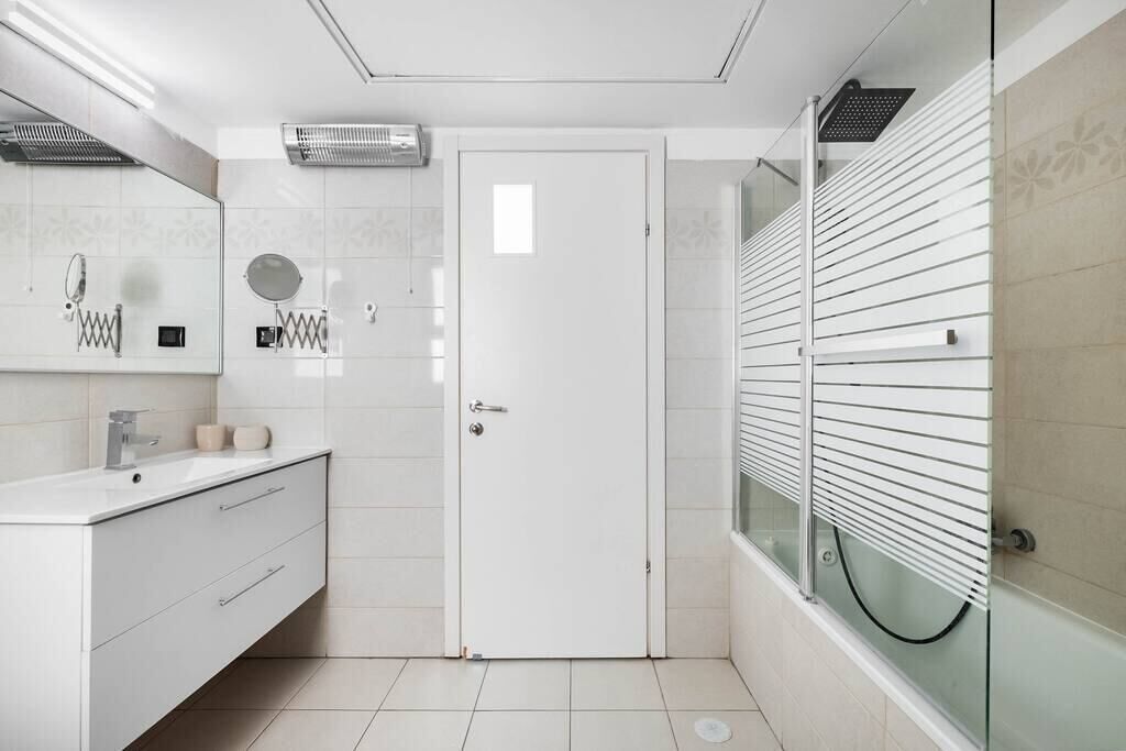 Ein modernes Badezimmer mit einem weißen Waschtisch, einer Glasdusche und einer Tür mit Griff.