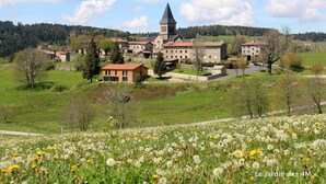 A historic building complex with a prominent tower, surrounded by lush green fields and a variety of trees.