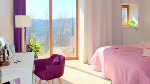A bedroom with a bed, a chair, a desk, and a window with curtains.