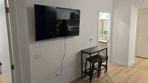 Una sala de estar moderna con un televisor de pantalla plana montado en la pared, una mesita de madera con dos sillas y un estante empotrado con un espejo.