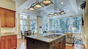Una cocina amplia con una isla grande, armarios de madera y vistas al exterior a través de ventanas grandes.