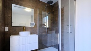 A modern bathroom with a white vanity, a large mirror, and a glass-enclosed shower area. - LOGIS DES COEVRONS (Évron)