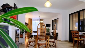 A dining area with wicker chairs and a table, a ceiling light, and a television on the wall. - LOGIS DES COEVRONS (Évron)