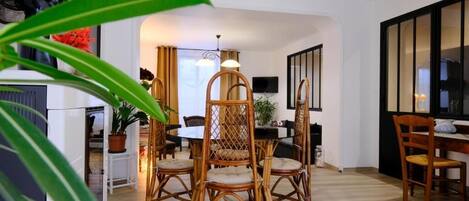 A dining area with wicker chairs and a table, a ceiling light, and a television on the wall.