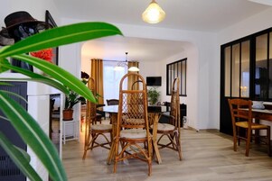 Un comedor con sillas de mimbre y una mesa, una lámpara en el techo y un televisor en la pared.