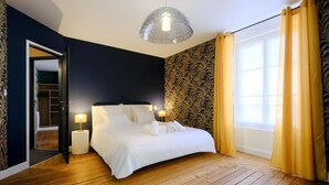 A bedroom with a large bed, a wardrobe, a mirror, and a window with curtains. - LOGIS DES COEVRONS (Évron)