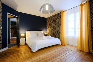 A bedroom with a large bed, a wardrobe, a mirror, and a window with curtains.