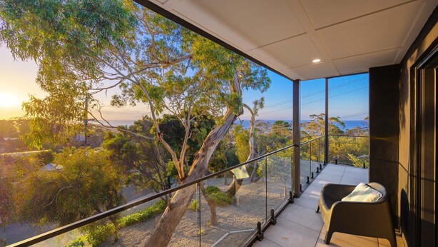 Un balcon doté d’une balustrade en verre, d’une chaise et offrant une vue sur les arbres et un paysage lointain.