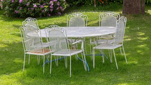 A white metal outdoor dining set with chairs and a table, surrounded by green grass and bushes.