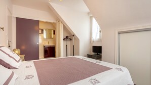 A bedroom with a bed, a TV, a wardrobe, and a bathroom visible through an open door.