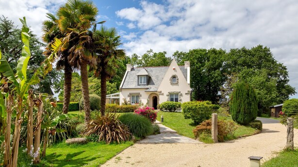A house with a gravel driveway, surrounded by lush greenery and a clear sky.