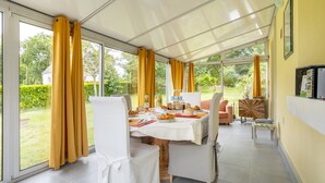 A conservatory with a dining table set for two, a sofa, and a television.