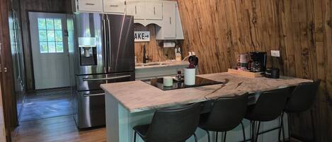 A modern kitchen with a stainless steel refrigerator, a built-in oven, and a bar area with stools.