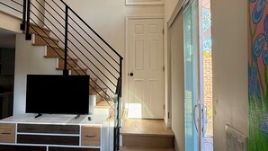 Un intérieur moderne avec un escalier, un téléviseur à écran plat posé sur une console blanche et une porte vitrée donnant sur l’extérieur.