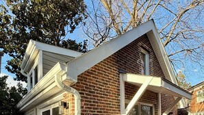Une maison à deux étages, construite en briques, avec un garage, de grandes fenêtres et une terrasse en pierre.