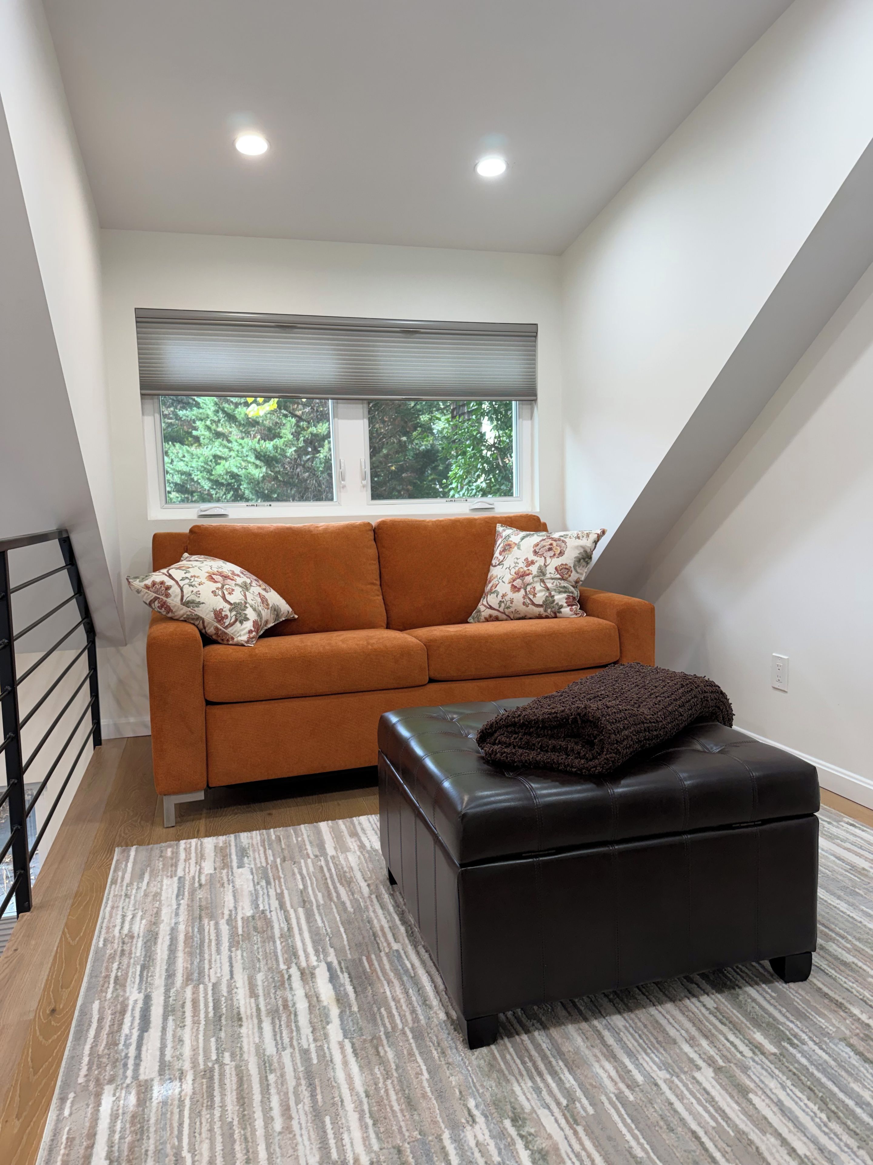 A modern living room with a sofa, ottoman, and a window with blinds.