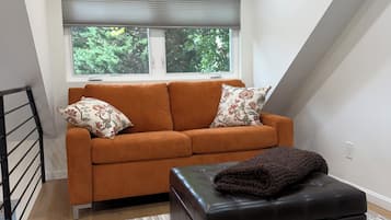 A modern living room with a sofa, ottoman, and a window with blinds.
