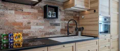 A kitchen with a brick wall, wooden cabinets, a black countertop, and a stainless steel oven.