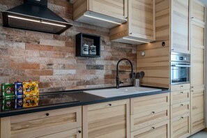 A kitchen with a brick wall, wooden cabinets, a black countertop, and a stainless steel oven.