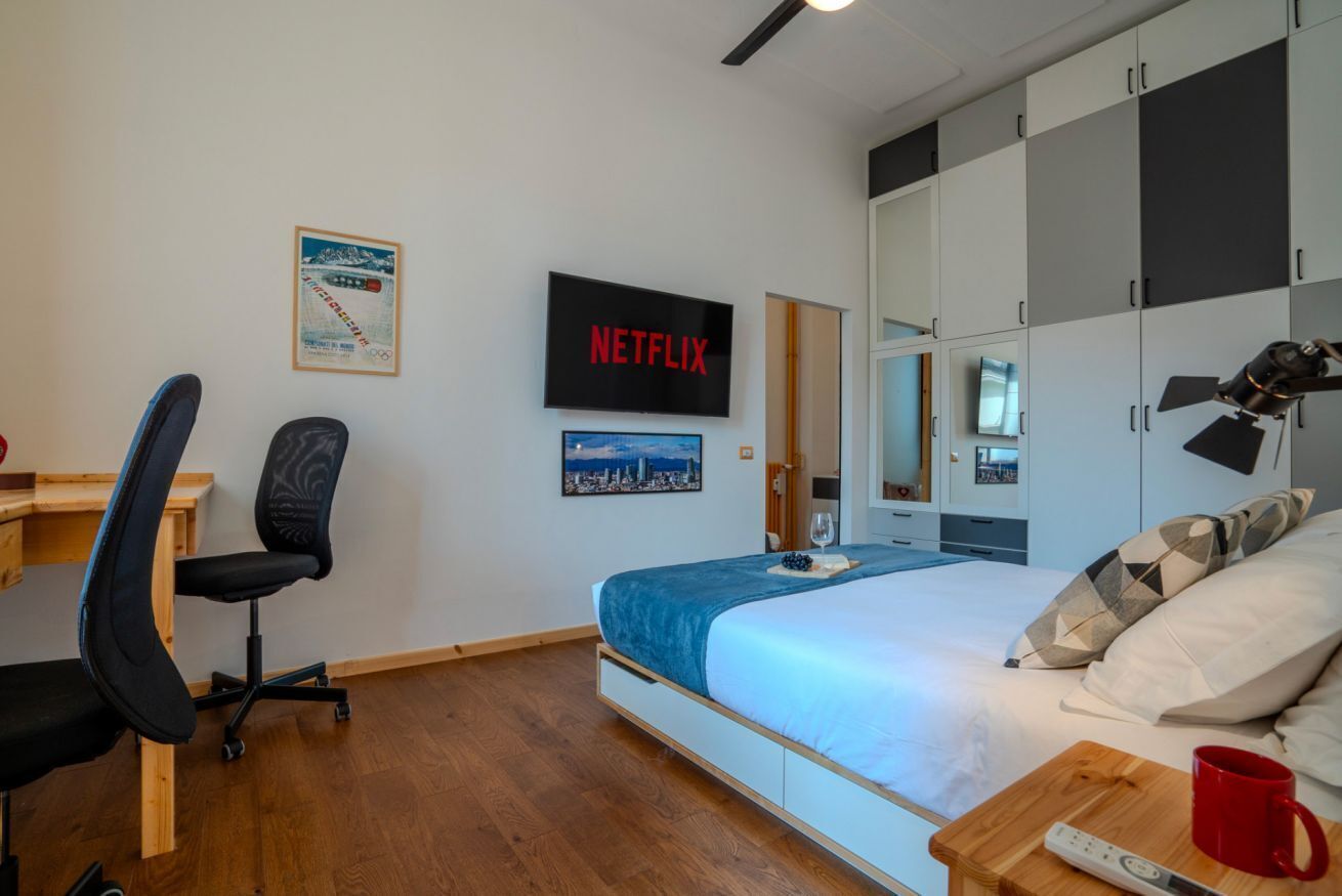 Un dormitorio con cama, escritorio, silla, televisor y armario.