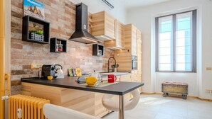 A modern kitchen with a brick wall, wooden cabinets, a black countertop, and a window. - GuestHost - Milanese Mountain Escape x5 (Milano)