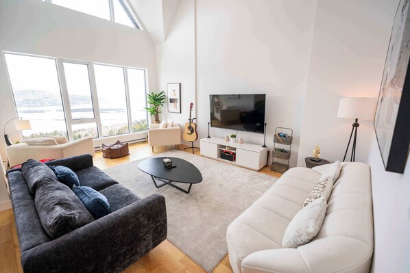 A modern living room with a sofa, coffee table, TV, and a view of the outdoors. - 403 | Luxury Condo | Incredible View & Pool (Baie-Saint-Paul)