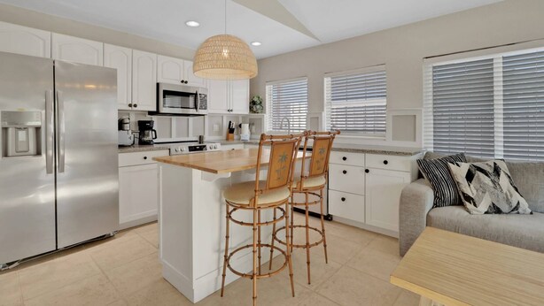 A modern kitchen with white cabinets, a central island with stools, a built-in oven, and a microwave. - 2589 Bayshore Dr (Matlacha)