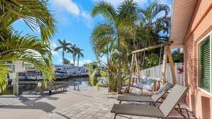 A patio with two lounge chairs, a swing set, and a view of a marina with boats. - 2589 Bayshore Dr (Matlacha)