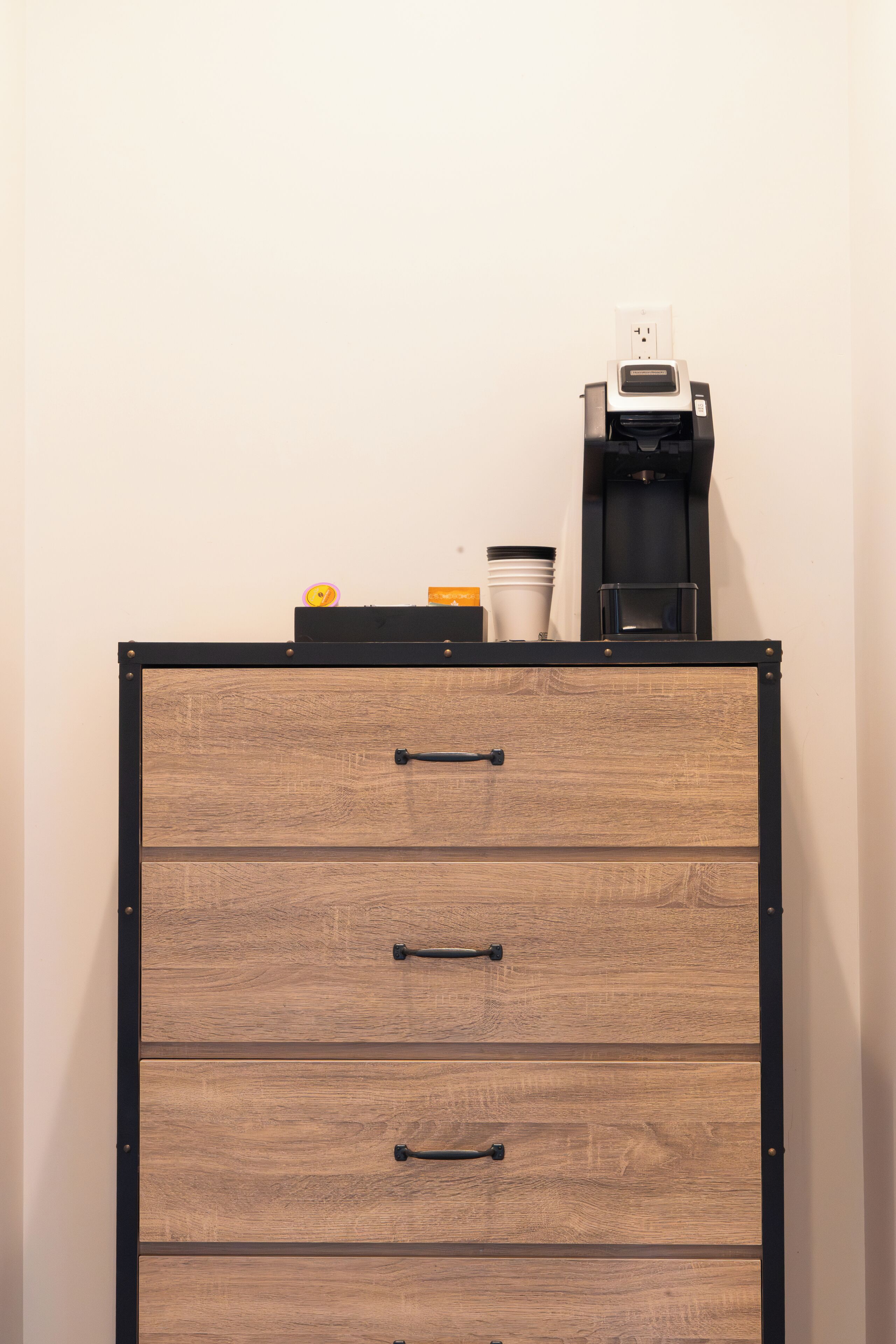 Un classeur en bois à quatre tiroirs, une machine à café et quelques tasses posées sur le dessus.
